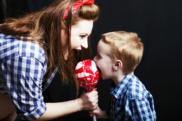 Fashionable redhead woman in pin up style  with her son with a lollipop in studio