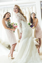Naklejka premium Young smiling bride and bridesmaids in wedding atelier