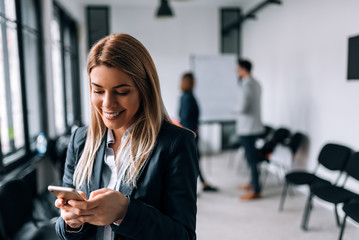 Smiling business woman using phone during a break. Collegues standing in the background