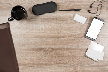 wooden desk with smartphone, headphones, name tag, pen, coffee mug, briefcase, case for eyeglasses and business cards in a metal case