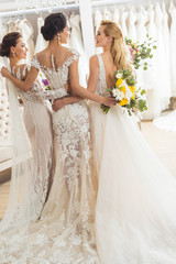 Naklejka premium Attractive women in wedding dresses embracing in wedding fashion shop