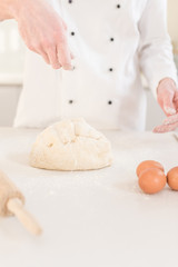 Men hands sprinkle a dough with flour close up. Man preparing bread dough