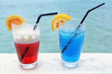Red and blue cocktail drinks with ice served on a poolside table in a tropical resort