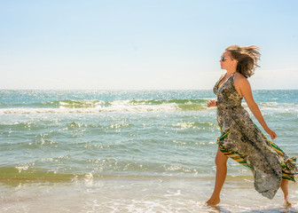 A pretty woman running along a black sea beach in a dress up against the sky