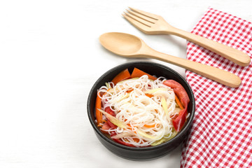 chinese rice noodles and vegetables salad in a ceramic bowl on white wooden board with copy space for text. homemade style food concpet.