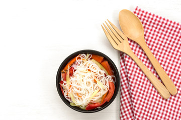 top view of chinese rice noodles and vegetables salad in a ceramic bowl on white wooden board with copy space for text. homemade style food concpet.
