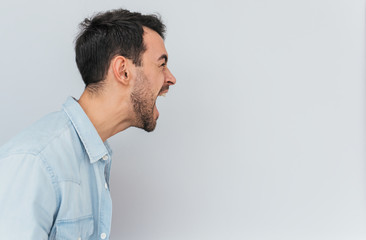 Obraz premium Side view portrait of emotional mad stylish young male screams loudly and with anger, being stressed, expresses negative emotions, isolated over white background. Emotions, feelings and people concept