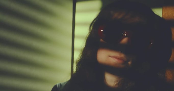 Light through window blinds frame a sad girl wearing red sunglasses. shot in slow motion