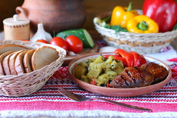 A plate with fried steak, stewed potatoes and baked bell pepper on a background of fresh vegetables.
