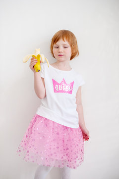 A girl in a bright skirt eating a banana