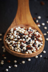 Mixed raw quinoa (Chenopodium quinoa). Red, black and white seeds in wooden spoon on black background
