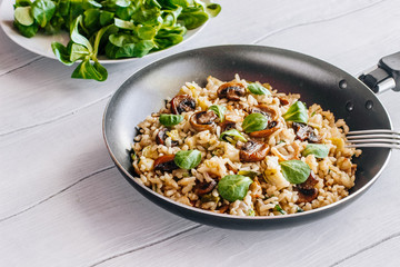 Fried rice with bacon, mushrooms and greens in a frying pan on a wooden table