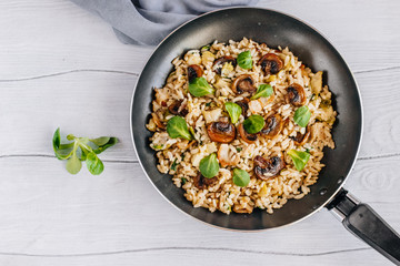 Risotto with bacon, mushrooms and greens in a frying pan on a wooden table