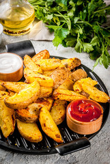 baked fried potatoes with garlic, herbs, red and white sauces, on grey stone background copy space