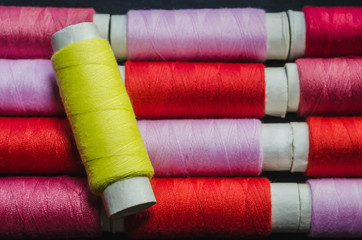 Spool of yellow thread on the background of spools of pink and red thread