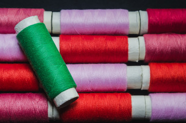 Spool of green thread on the background of spools of pink and red thread