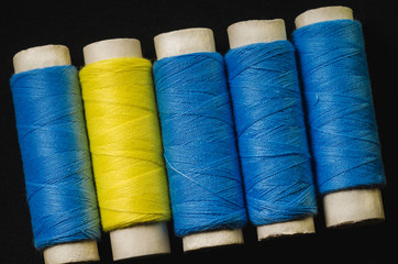 Spools of blue and yellow sewing thread on black material
