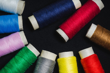 Spools of colored sewing thread on black material