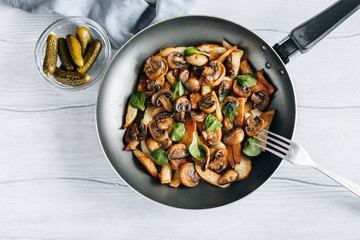 Fried potatoes with mushrooms and greens in a frying pan on a wooden table vegetarian food top view
