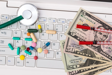 On the keyboard - stethoscope, dollars, pills and syringe