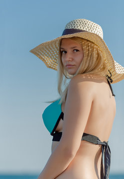 Waist-up portrait of young woman in straw hat and swimsuit