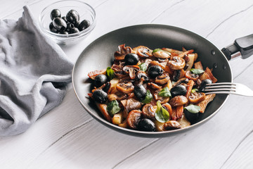 Fried potatoes with mushrooms, olives and greens in a frying pan on a wooden table vegetarian food