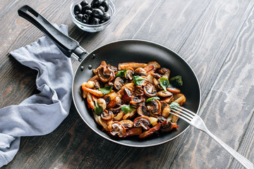 Fried potatoes with mushrooms and greens in a frying pan on a wooden table vegetarian food