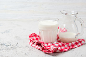 Glass and jug of milk and checkered towel on wooden background