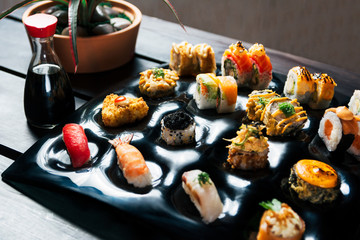 Rainbow Sushi Roll with salmon, eel, tuna, avocado, royal prawn, cream cheese Philadelphia, caviar tobica, chuka. Sushi menu on a black wood background closeup.