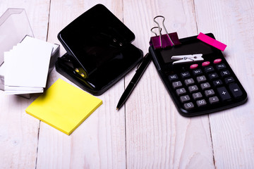 Stationery and calculator. Hole punch near pen on wooden background.