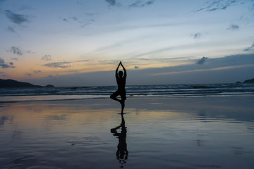 Silhouette of a asian man acts yoga on the beach when twilight. Sunset sky background