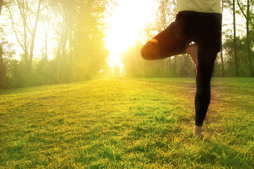 leg of woman in sport suit posing in tree yoga on the green grass garden with summer sun light morning background