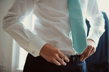 Grooms morning preparation, handsome groom getting dressed and preparing for the wedding, wearing a belt.