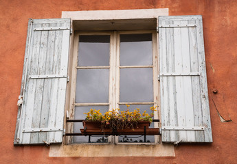 Old typical Mediterranean house with ocher stucco wall, wooden shutters and yellow flowers on the...