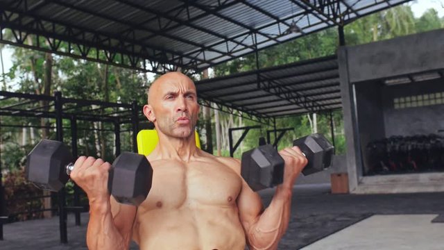 Face bodybuilder lifting dumbbells during training muscles on body in gym club