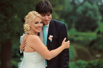 Bride and groom at wedding Day walking Outdoors on summer nature. Bridal couple, Happy Newlywed woman and man embracing in green park. Loving wedding couple outdoor. Bride and groom in honeymoon