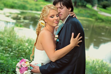 Bride and groom at wedding Day walking Outdoors on summer nature. Bridal couple, Happy Newlywed woman and man embracing in green park. Loving wedding couple outdoor. Bride and groom in honeymoon