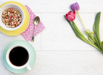 Looking down from above onto a feminine Breakfast Flat Lay table with black coffee, muesli or granola and flowers on a white background.