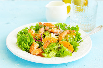 A plate of lettuce, with slices of orange, red onion, with vinaigrette dressing.