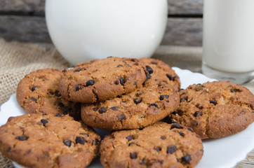 Oatmeal chocolate chip cookies, jug and glass of milk, rustic wooden background.