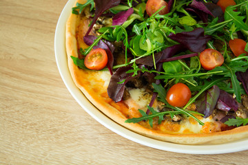 Pizza with arugula, salad mix and cherry tomatoes on wooden table