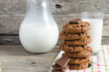 Oatmeal chocolate chip cookies, jug and glass of milk, rustic wooden background.