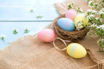 Colorful Easter eggs in nest with flowers on blue wooden background.  Easter holiday in spring season, top view with composition.