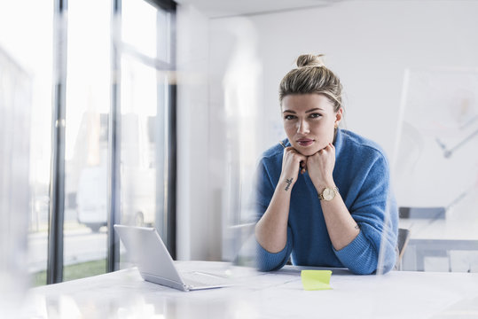 Portrait of young woman with laptop at desk in office