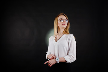 Studio portrait of blonde businesswoman in glasses, white blouse and black skirt against dark background. Successful woman and stylish girl concept.