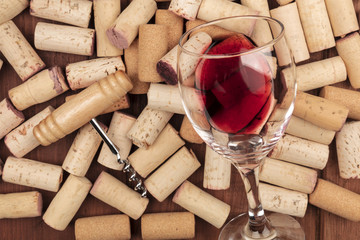 A closeup of a glass of red wine with a corkscrew on top of many wine corks