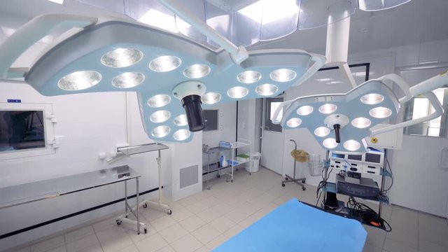 A couple of surgical lamps hanging above the operation table is getting switched on