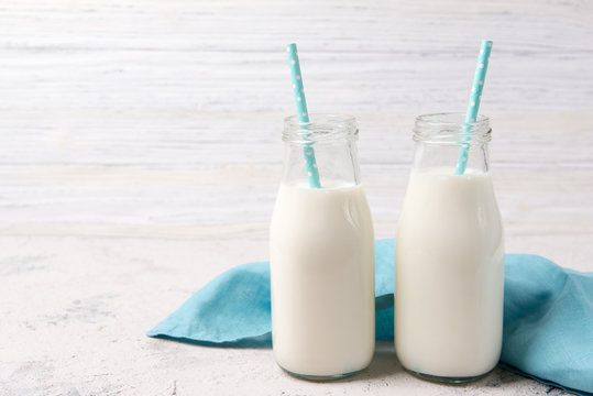 Two bottles of milk with blue straws on wooden background