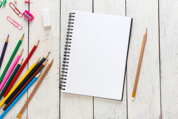 Empty notebook and colorful pencils on white wooden table