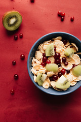 Delicious crispy cornflakes with kiwi pieces, almonds and cranberries in bowl, healthy breakfast on red background